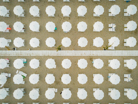 Aerial view of rows of white beach umbrellas and sun loungers arranged on the sandy beach in San Benedetto del Tronto, Marche, Italy.