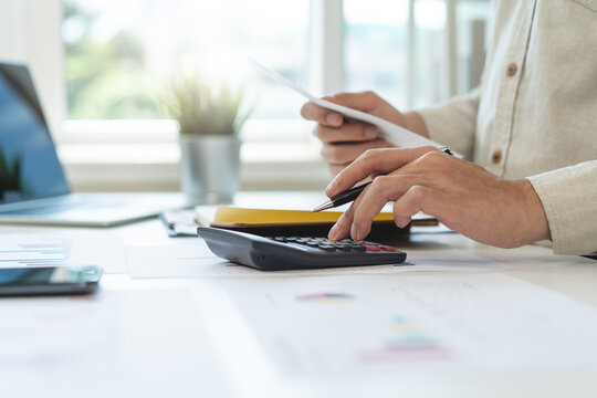 Deduction planning, debt asian accountant hand using calculator to calculating money balance from bill and income, cost budget expenses for pay money form personal individual on table at home.