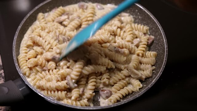 Fusilli pasta cooking in creamy mushroom sauce in pan. Close up of creamy fusilli dish with mushroom sauce.