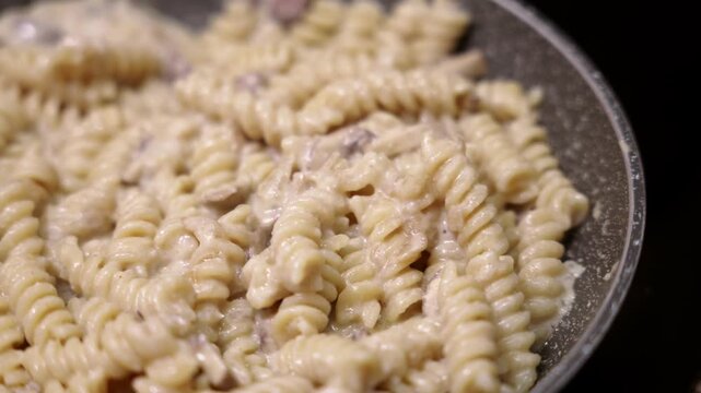Fusilli pasta cooking in creamy mushroom sauce in pan. Close up of creamy fusilli dish with mushroom sauce.