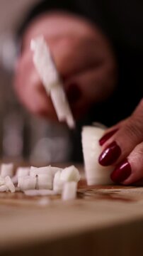 Dicing onion with knife on wooden cutting board close-up. Woman chopping fresh onion in dice with knife.