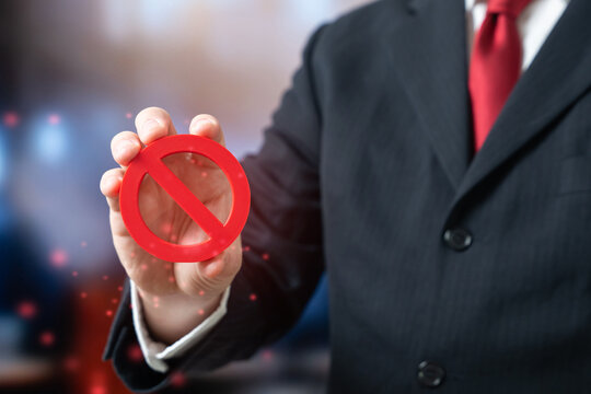 A businessman holds a red NO prohibition sign. Rules and restrictions. New directives. Concept of corporate policy enforcement and compliance in modern business management.