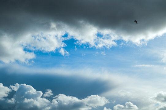 Dramatic sky landscape background with dark grey storm clouds and a small bird flying at the distance