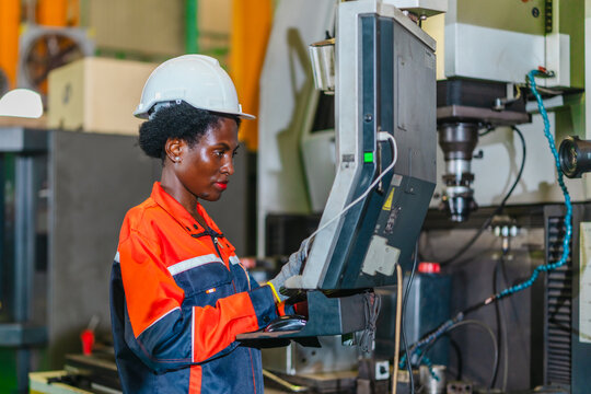 African woman machine operator inspecting metal part at CNC machine in automotive parts factory