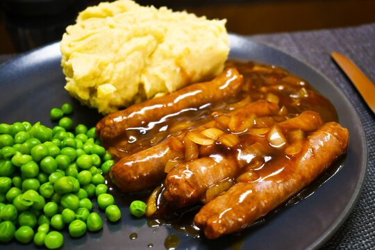 Bangers beef sausages in gravy sauce with peas and mashed potatoes on a plate. Western food style.