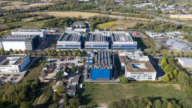 Aerial view of a large data center complex featuring multiple industrial buildings with rooftop cooling units, parking areas, and surrounding green landscape Frankfurt am Main, Hessen, Germany.