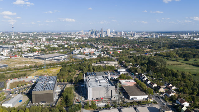 Aerial view of industrial buildings and warehouses in the foreground with the Frankfurt am Main skyline visible in the distance in Frankfurt am Main, Hessen, Germany.