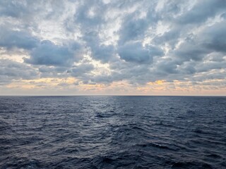 Obraz premium Dramatic cloudy sky over calm ocean at dusk with golden horizon glow. Moody seascape background.