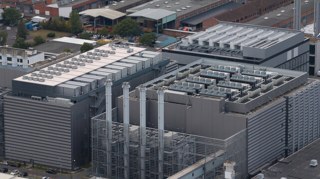 Aerial view of a large data center with multiple cooling units on the roof, tall ventilation chimneys, and metal facade structures in Frankfurt am Main, Hessen, Germany.