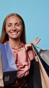 Portrait of smiling young adult Caucasian woman holding multiple shopping bags on shoulders. Ideal footage for retail promotions, seasonal sales campaigns, Black Friday marketing, vertical