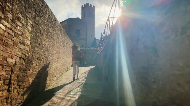 Woman walking towards historic basilica Cateriniana San Domenico under sunset sunlight in Siena, Italy