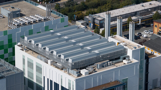 Aerial view of a modern industrial building featuring large rooftop HVAC units, a white facade with green accents, and industrial chimneys in Frankfurt am Main, Hessen, Germany.