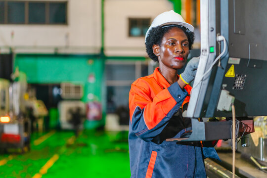 African woman machine operator inspecting metal part at CNC machine in automotive parts factory