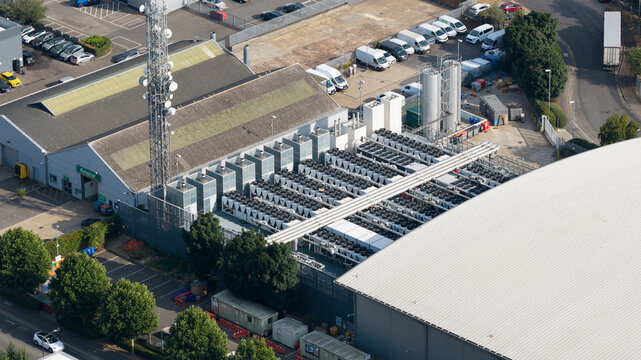 Aerial view of an industrial facility featuring large rooftop cooling units, a communication tower, and adjacent warehouse buildings in Slough, England, United Kingdom.