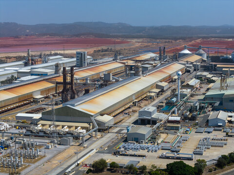 Aerial view of Boyne Smelter, a large industrial aluminum facility with long metal-roofed buildings, storage tanks, and red earth landscape in Boyne Island, Queensland, Australia.