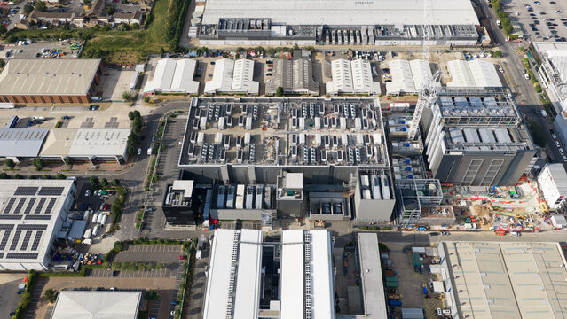 Aerial view of a large industrial data center complex featuring numerous rooftop cooling units, a construction crane, and surrounding warehouses in Slough, England, United Kingdom.