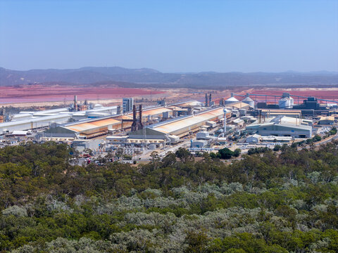 Aerial view of the Boyne Smelter industrial facility featuring large metal-roofed buildings surrounded by native eucalyptus forest and red earth landscape in Boyne Island, Queensland, Australia.