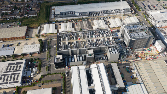 Aerial view of a large data center complex with industrial buildings, rooftop HVAC units, and construction cranes in an industrial area in Slough, England, United Kingdom.