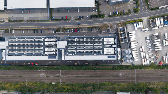 Aerial view of a large industrial facility featuring numerous rooftop HVAC units, a parking lot with vehicles, and adjacent railway tracks in Slough, England, United Kingdom.