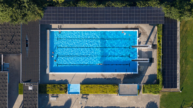 Aerial view of an outdoor swimming pool with lanes and diving boards, surrounded by a building with solar panels on the roof in Lauwerzijl, Groningen, Netherlands.