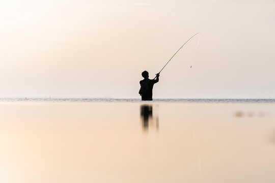 Pescador en la playa un amanecer con barco de fondo y el mar en calma