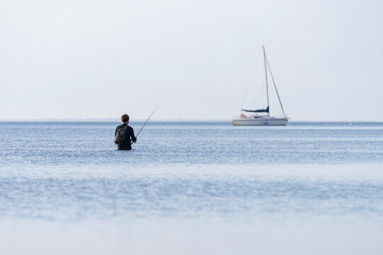 Pescador en la playa un amanecer con barco de fondo y el mar en calma