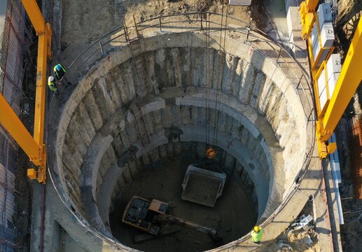 Aerial view of a deep circular construction excavation site with an excavator, a crane, and workers in safety gear in Bursa, Bursa, Turkiye.