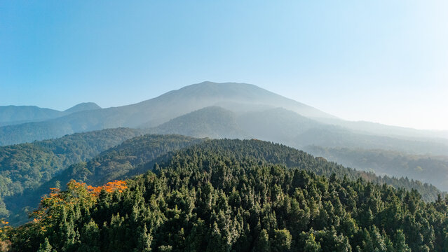 Aerial view of Mount Gede surrounded by dense evergreen forests and rolling hills under a clear blue sky in West Java, Indonesia.