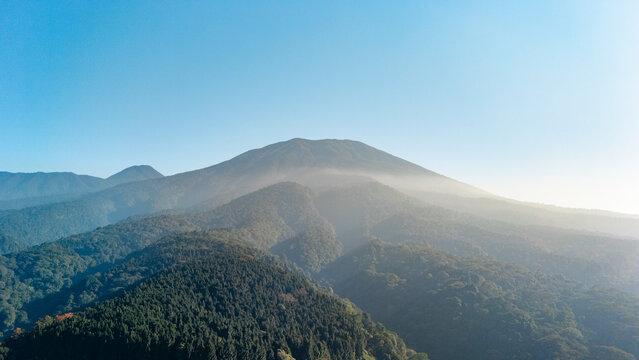 Aerial view of Mount Gede surrounded by lush forests and light mist under a clear blue sky in West Java, Indonesia.