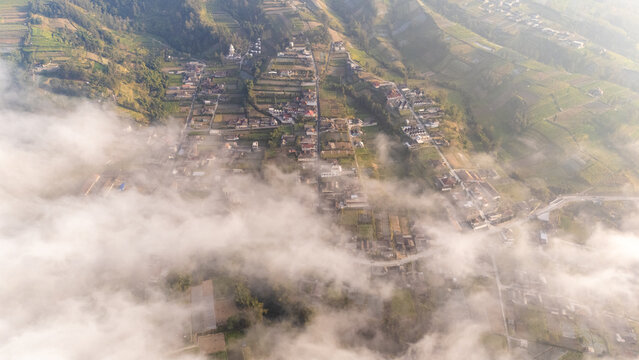 Aerial view of the village of Selo nestled in the mountainous landscape of Central Java with terraced fields and houses partially obscured by morning clouds, Selo, Central Java, Indonesia.