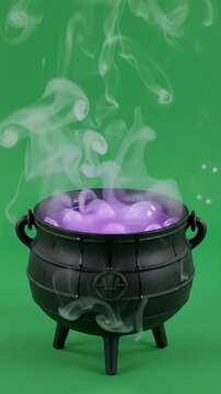 Black Cast Iron Witch Cauldron Bubbling with Purple Potion and Smoke - An antique-style black cast iron cauldron sits on a green background, bubbling with a mystical purple potion.