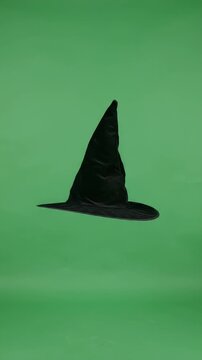 Pointed Black Velvet Witch Hat Floating on Green Screen - A classic pointed black velvet witch hat floats against a solid green screen background, isolated for easy compositing.