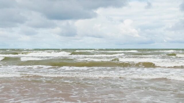 Ocean waves rolling onto beach under cloudy sky