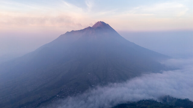 Aerial view of Mount Merapi rising above a sea of clouds at sunrise with volcanic slopes and misty atmosphere in Selo, Central Java, Indonesia.