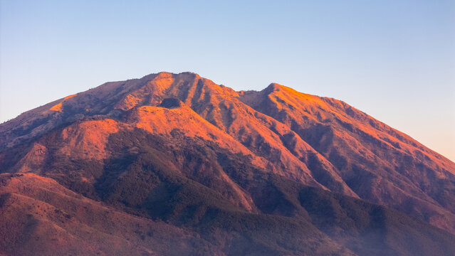 Aerial view of the rugged volcanic slopes of Mount Merbabu illuminated by golden hour light in Selo, Central Java, Indonesia.