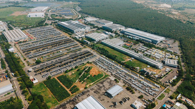 Aerial view of a large truck factory featuring extensive parking lots filled with numerous commercial vehicles, industrial warehouses, and surrounding green landscapes in India.