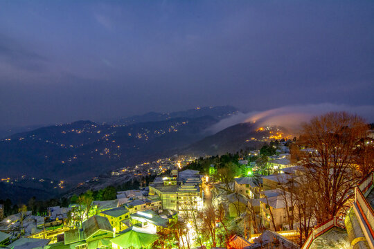 Aerial view of the snow-covered town illuminated at night with mountain slopes and fog in the background in Murree, Punjab, Pakistan.