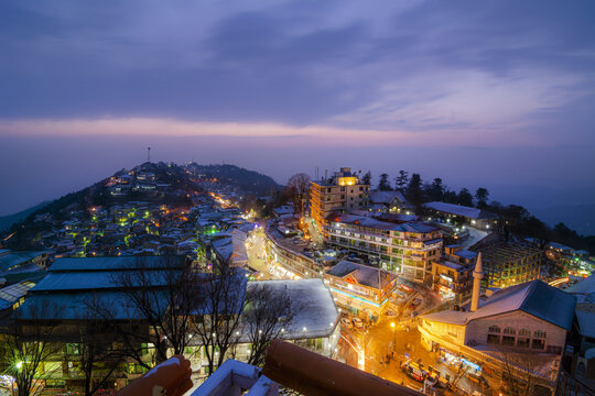 Aerial view of the hill station at dusk with illuminated buildings and snow-covered rooftops nestled in the mountains of Murree, Punjab, Pakistan.