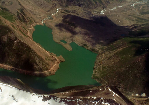 Aerial view of Lulusar Lake surrounded by rugged mountains, winding dirt roads, and snow-capped peaks in the high-altitude landscape of Balakot, Khyber Pakhtunkhwa, Pakistan.