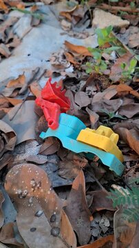 Discarded colorful plastic toy parts abandoned among dry leaves on the ground for environmental pollution and plastic waste concept