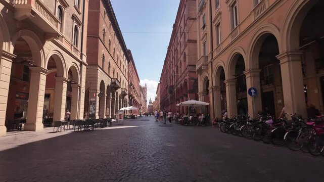 Pedestrian street with historic porticos and cafe seating, Bologna, Italy