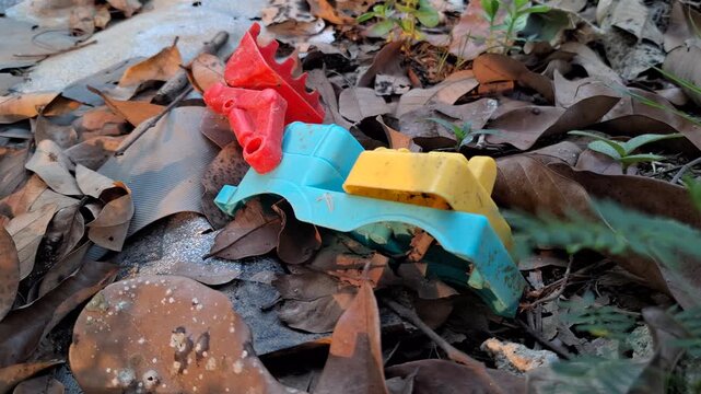 Discarded colorful plastic toy parts abandoned among dry leaves on the ground for environmental pollution and plastic waste concept