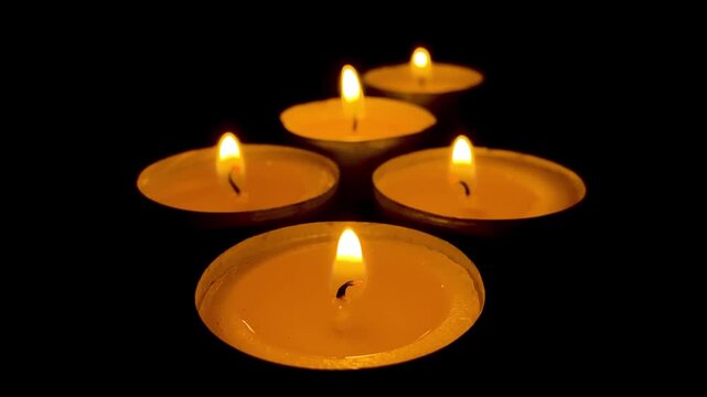 Group of small burning tealight candles glow with warm flame in dark room