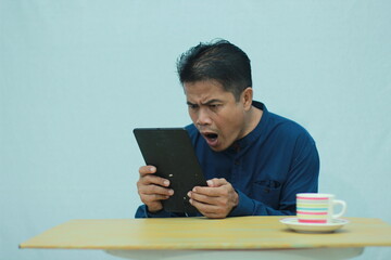 Shocked adult man looking at a tablet screen with a surprised expression after seeing unexpected information. © Dian