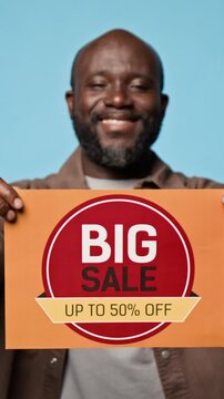 Portrait of smiling African American man holding promotional big sale discount banner. Footage suitable for retail marketing, shopping clearance campaigns, vertical