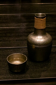 Traditional metal sake bottle and cup on a wooden table at Takefue ryokan, Aso District, Kumamoto, Japan