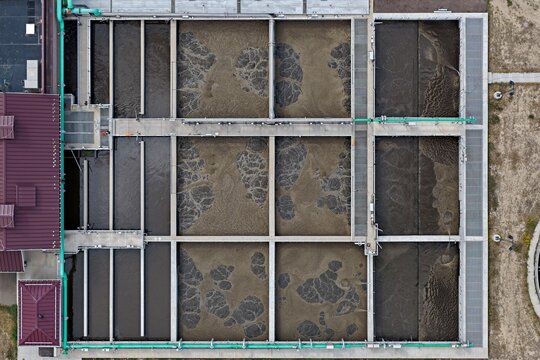 Aerial view of the wastewater treatment plant featuring large rectangular aeration tanks with bubbling water and industrial piping in Erie, Colorado, United States.