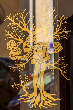 The golden emblem of the historic institution Accademia dei Rozzi in Siena, Italy, founded in the 16th century. A tree bearing the famous motto "Whoever stays here gains what he loses."