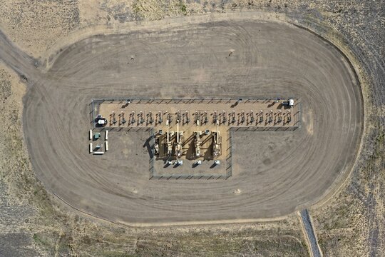 Aerial view of an oil well pad with pump jacks and storage tanks surrounded by a dirt access road in Erie, Colorado, United States.