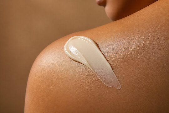 A doll's shoulder is being applied with a dab of light-colored cream.